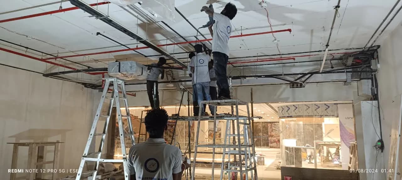 ESEA technicians on ladders fixing electrical conduit along a commercial ceiling